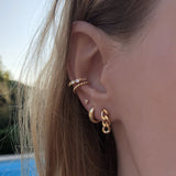 A female model’s ear showcasing several gold stud earrings, hoops and an ear cuff.
