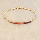 Original Kurafuchi bracelet made of two thin gold chains. One strand is decorated with beads in a burgundy to gold gradient.