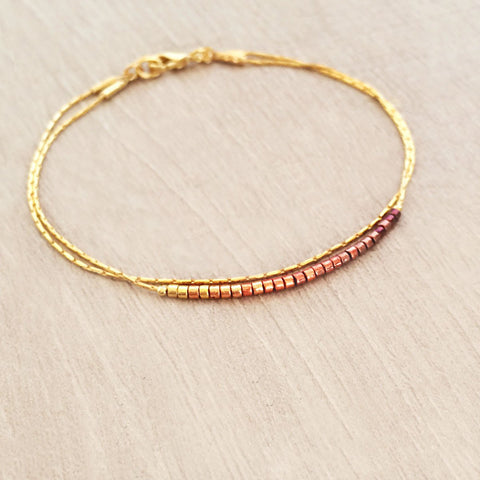 Original Kurafuchi bracelet made of two thin gold chains. One strand is decorated with beads in a burgundy to gold gradient.