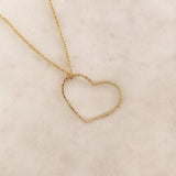 A photo of a gold necklace made of dainty chains with a large hammered heart pendant.