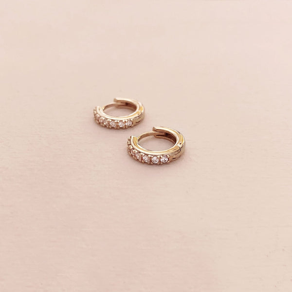 A pair of small gold hoop earrings paved with little zircon crystals. By Kurafuchi.