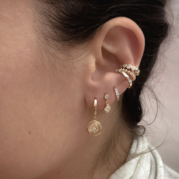 A female model’s ear showcasing several gold stud earrings, hoops and an ear cuff, all by Kurafuchi.