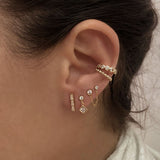 A female model’s ear showcasing several gold stud earrings and ear cuffs.