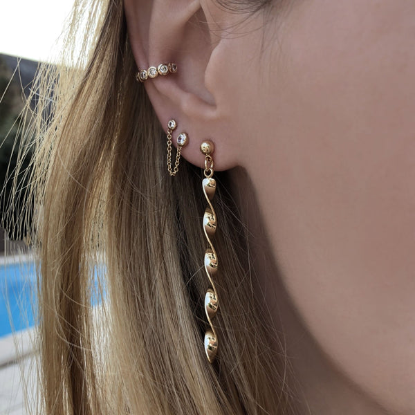 A female model’s ear featuring several gold stud earrings and an ear cuff.