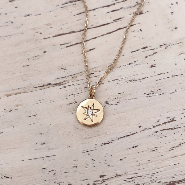 Lovely pendant necklace featuring a small round medal charm adorned with a star design and centered with a zircon crystal.