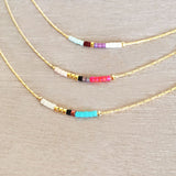 Minimalist necklace made of a dainty gold chain decorated with tiny beads in a colorful pattern. Designed by Kurafuchi.