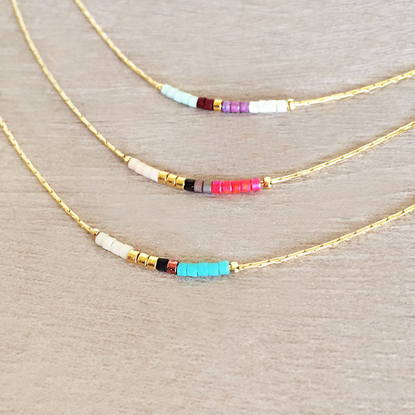 Minimalist necklace made of a dainty gold chain decorated with tiny beads in a colorful pattern. Designed by Kurafuchi.