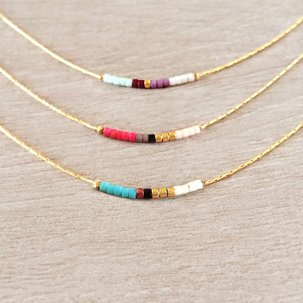 Minimalist necklaces made of a thin gold chain decorated with tiny beads in a colorful pattern. Designed by Kurafuchi.