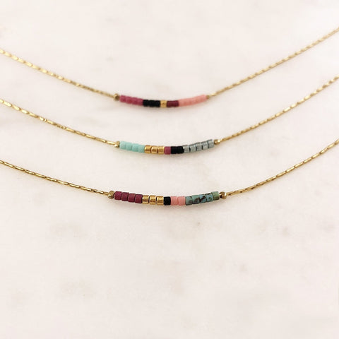 Minimalist necklaces made of a dainty gold chain decorated with tiny beads in a colorful pattern. Designed by Kurafuchi.