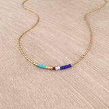 Minimalist necklace made of a dainty gold chain decorated with tiny beads in a colorful pattern. Designed by Kurafuchi.