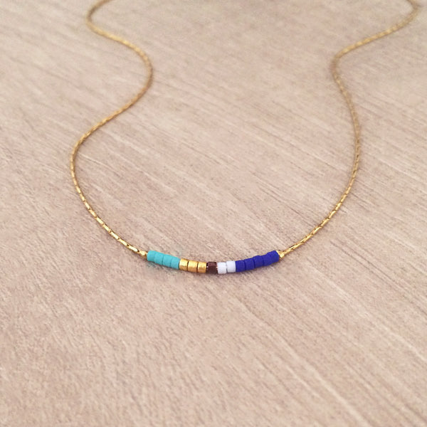 Minimalist necklace made of a dainty gold chain decorated with tiny beads in a colorful pattern. Designed by Kurafuchi.
