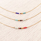 Minimalist necklaces made of a dainty gold chain decorated with tiny beads in a colorful pattern. Designed by Kurafuchi.