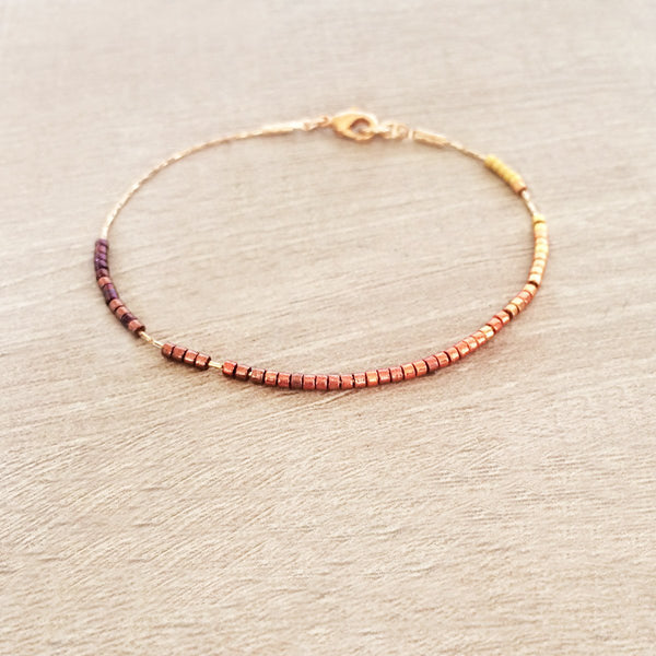 Dainty bracelet by Kurafuchi Jewelry, featuring a thin chain decorated with small beads in a gold to burgundy gradient.