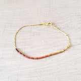 Dainty bracelet by Kurafuchi Jewelry, featuring a thin chain decorated with small beads in a gold to burgundy gradient.