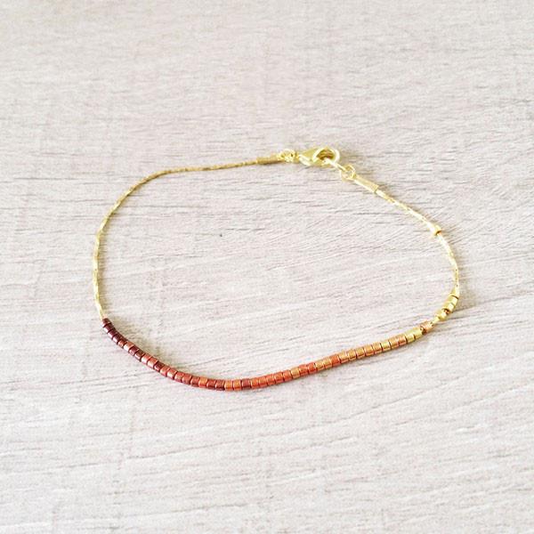Dainty bracelet by Kurafuchi Jewelry, featuring a thin chain decorated with small beads in a gold to burgundy gradient.