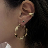 A female model’s ear featuring several Kurafuchi gold stud earrings, hoops and an ear cuff.