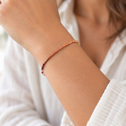 Dainty bracelet by Kurafuchi Jewelry, featuring a thin chain decorated with small beads in a gold to burgundy gradient.