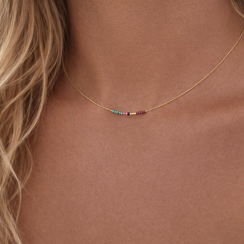 Minimalist necklaces made of a dainty gold chain decorated with tiny beads in a colorful pattern. Designed by Kurafuchi.
