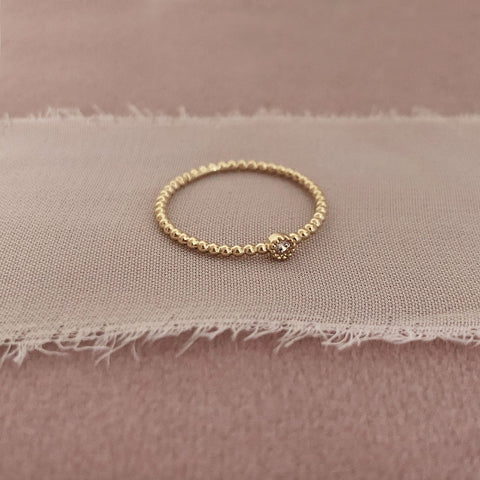 Dainty gold ring made of a thin beaded band decorated with a small zircon crystal.