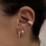 A female model’s ear showcasing several gold stud earrings, hoops and an ear cuff.