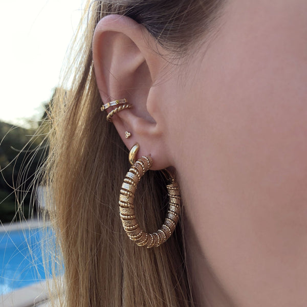A female model’s ear showcasing several gold stud earrings, hoops and an ear cuff.