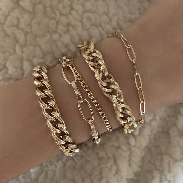 A female model’s wrist showcasing a layered look of multiple gold bracelets in various designs and thicknesses.