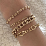 A female model’s wrist showcasing a layered look of multiple gold bracelets in various designs and thicknesses.