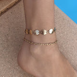 A female model’s ankle featuring two gold ankle bracelets.