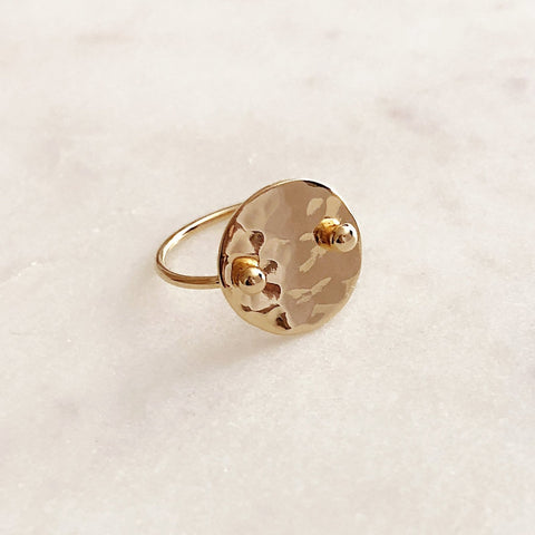 Photo of a gold ring by Kurafuchi Jewelry. The ring features a round disc with a hammered finish, on a dainty band.