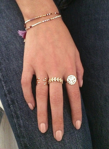A female model’s hand wearing a layered look of multiple Kurafuchi gold rings over several fingers.
