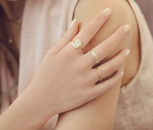 A female model’s hand showcasing a layered look of multiple gold rings over several fingers.