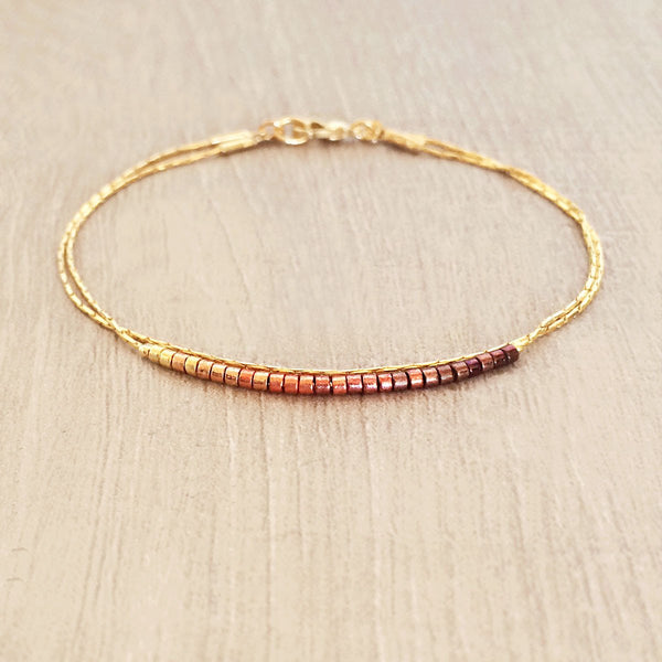 Original Kurafuchi bracelet made of two thin gold chains. One strand is decorated with beads in a burgundy to gold gradient.