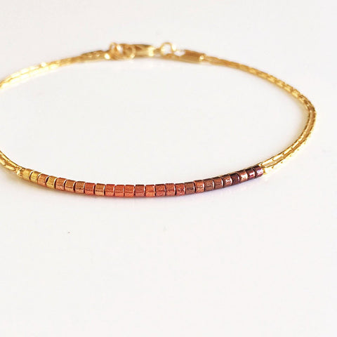 Original Kurafuchi bracelet made of two thin gold chains. One strand is decorated with beads in a burgundy to gold gradient.