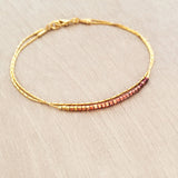 Original Kurafuchi bracelet made of two thin gold chains. One strand is decorated with beads in a burgundy to gold gradient.