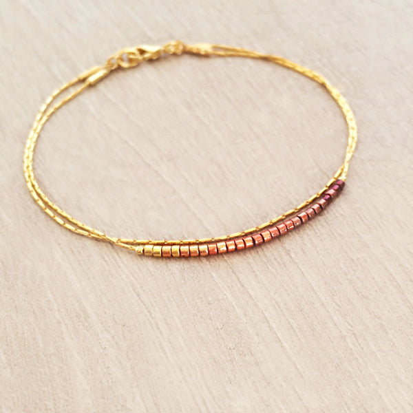 Original Kurafuchi bracelet made of two thin gold chains. One strand is decorated with beads in a burgundy to gold gradient.