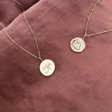 A photo of two gold Kurafuchi pendant necklace. The round medals feature egyptian symbols and measure 15mm in diameter.