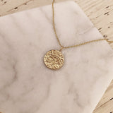 A photo of a gold pendant necklace. The round medal features an eye of Horus egyptian symbol and measures 15mm in diameter.