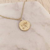 A photo of a gold pendant necklace. The round medal features an eye of Horus egyptian symbol and measures 15mm in diameter.