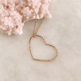 A photo of a rose gold necklace made of dainty chains with a large hammered heart pendant.