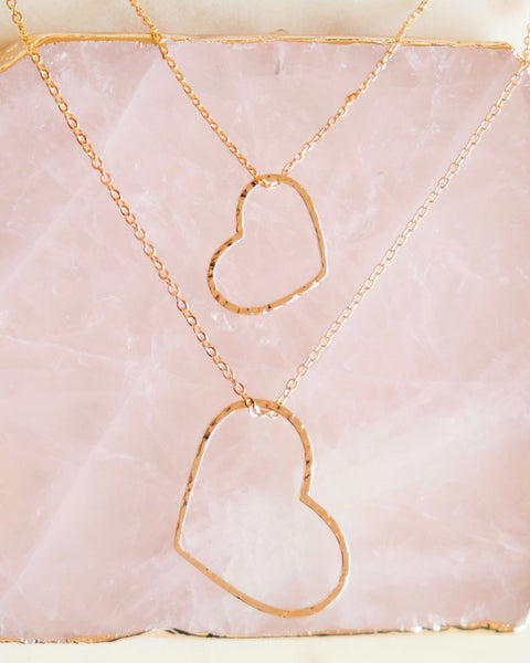 A photo of two necklaces made of dainty chains in gold and rose gold featuring pendants in a heart outline.