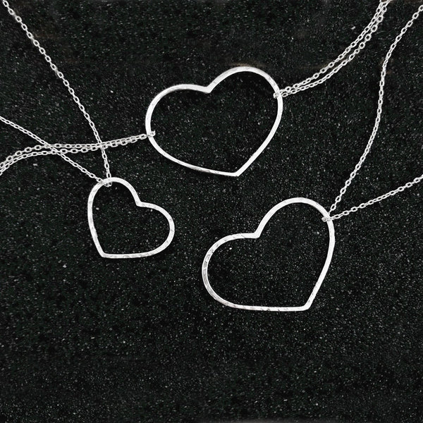 A photo of two silver necklaces and a bracelet made of dainty chains featuring pendants in a heart outline.