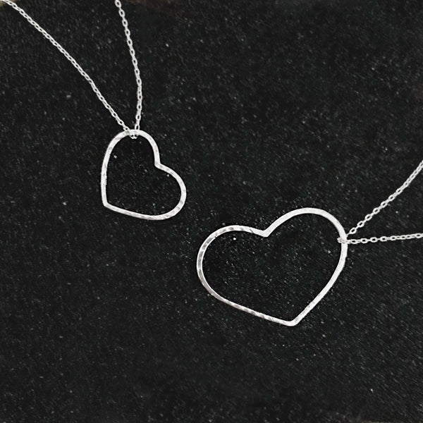 A photo of two silver necklaces made of dainty chains featuring pendants in a heart outline, one large and one small.