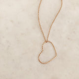 A photo of a gold necklace made of dainty chains with a large hammered heart pendant.