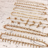 A photo of multiple gold ankle bracelets in various chain designs, laying on a wooden table.