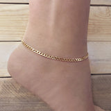 A female model’s ankle showcasing a gold anklet made of a flat curb chain with a mirror finish.