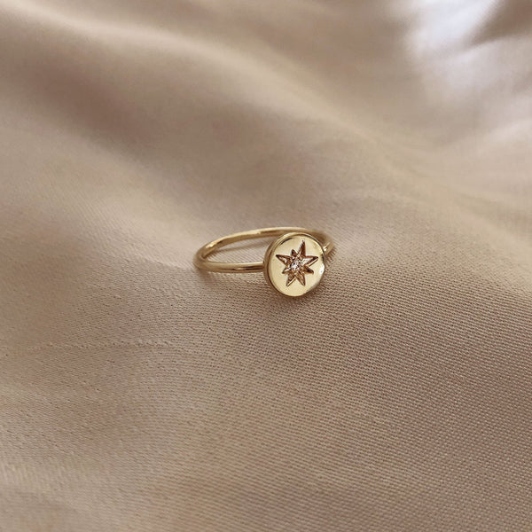 Dainty gold ring featuring a medal with a star design in its center, adorned with a tiny zircon crystal.