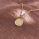 Pretty necklace featuring a dainty gold beaded chain and a round medal pendant engraved with a lotus design. By Kurafuchi.