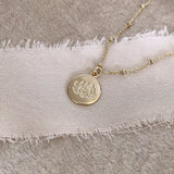 Pretty necklace featuring a dainty gold beaded chain and a round medal pendant engraved with a lotus design. By Kurafuchi.