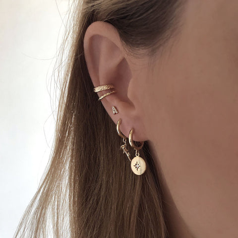 A pair of small hoop earrings adorned with gold medals with an engraved star. The star has a zircon crystal in its center.