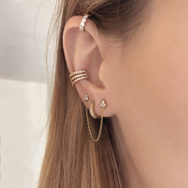 A female model’s ear featuring several Kurafuchi gold stud earrings, hoops and an ear cuff.